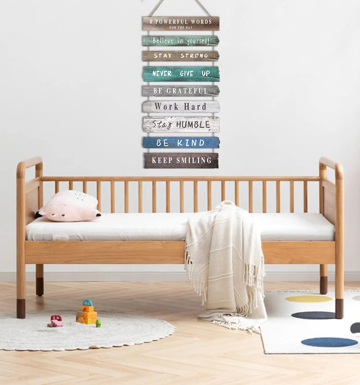 A rustic wooden wall art featuring motivational phrases in varied colors and textures hanging above a light wood crib.