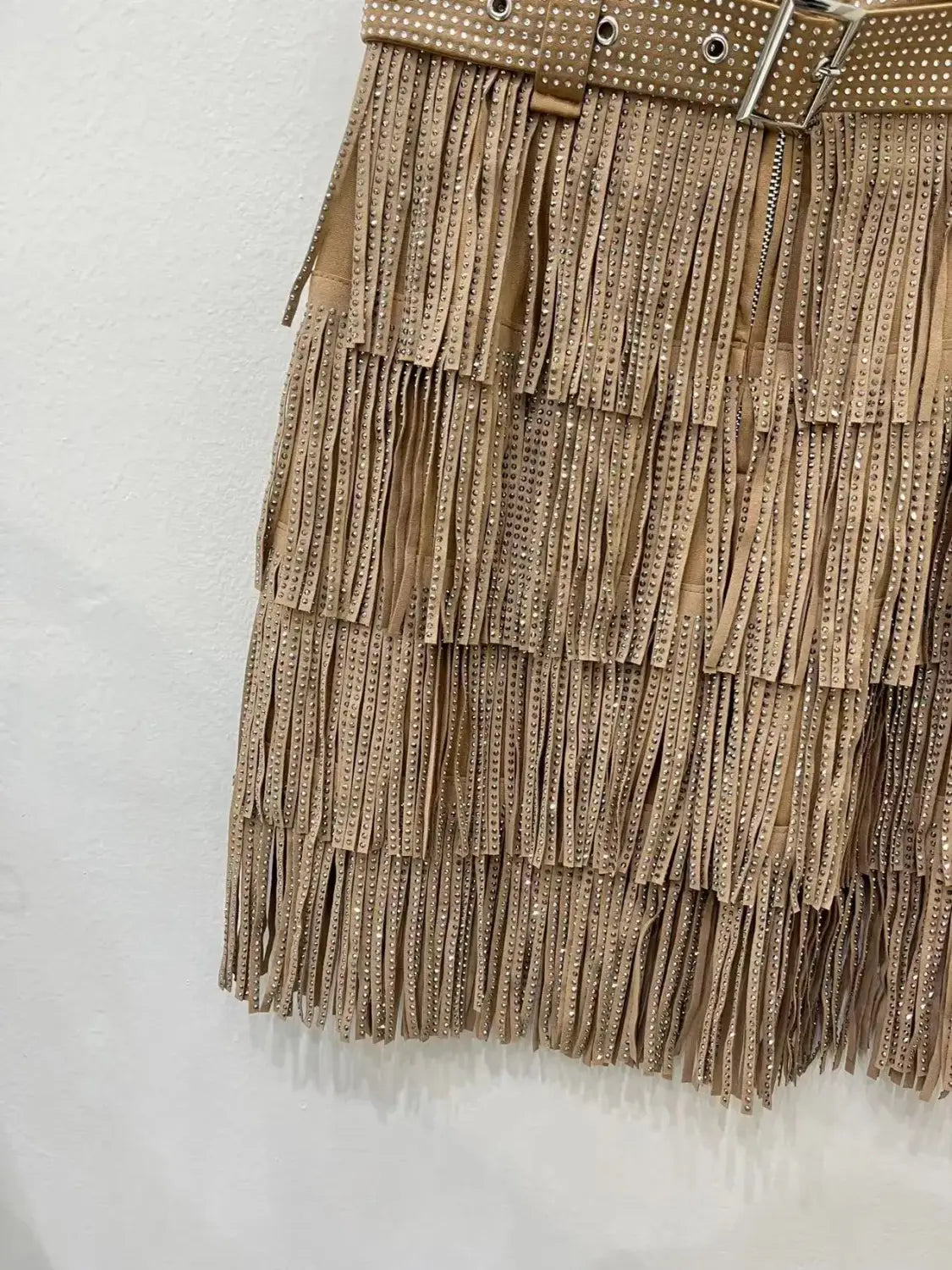 Mini-jupe taille haute en suède beige à franges en strass, avec ceinture à rivets et quincaillerie à tonalité argentée.