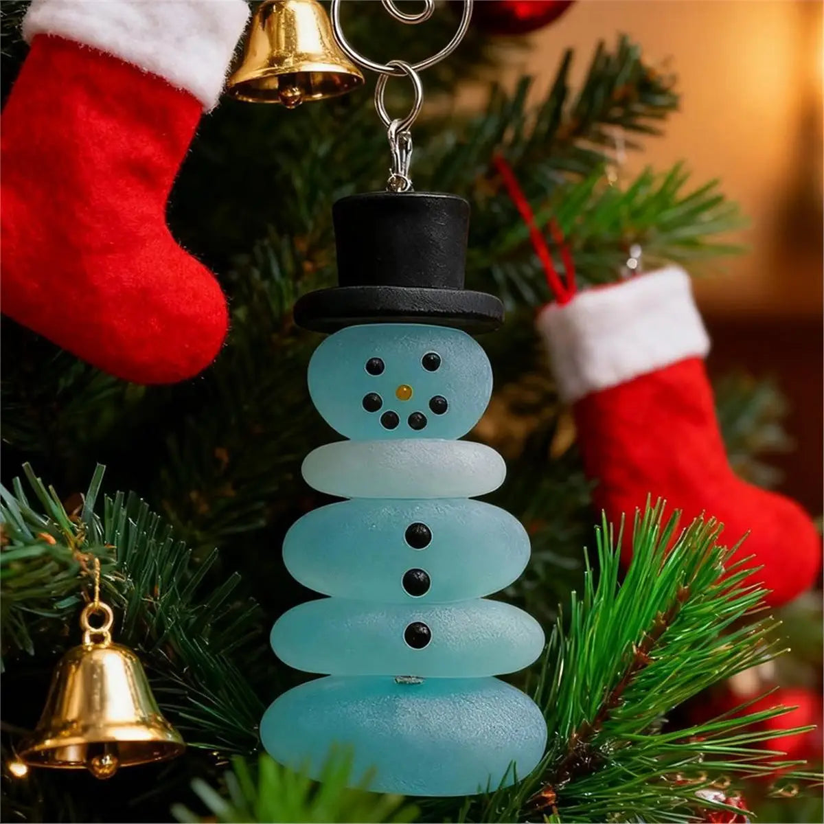 a light blue sea glass snowman christmas ornament with black button eyes and nose wearing a black top hat hanging from a silver keychain for christmas coastal tree decor