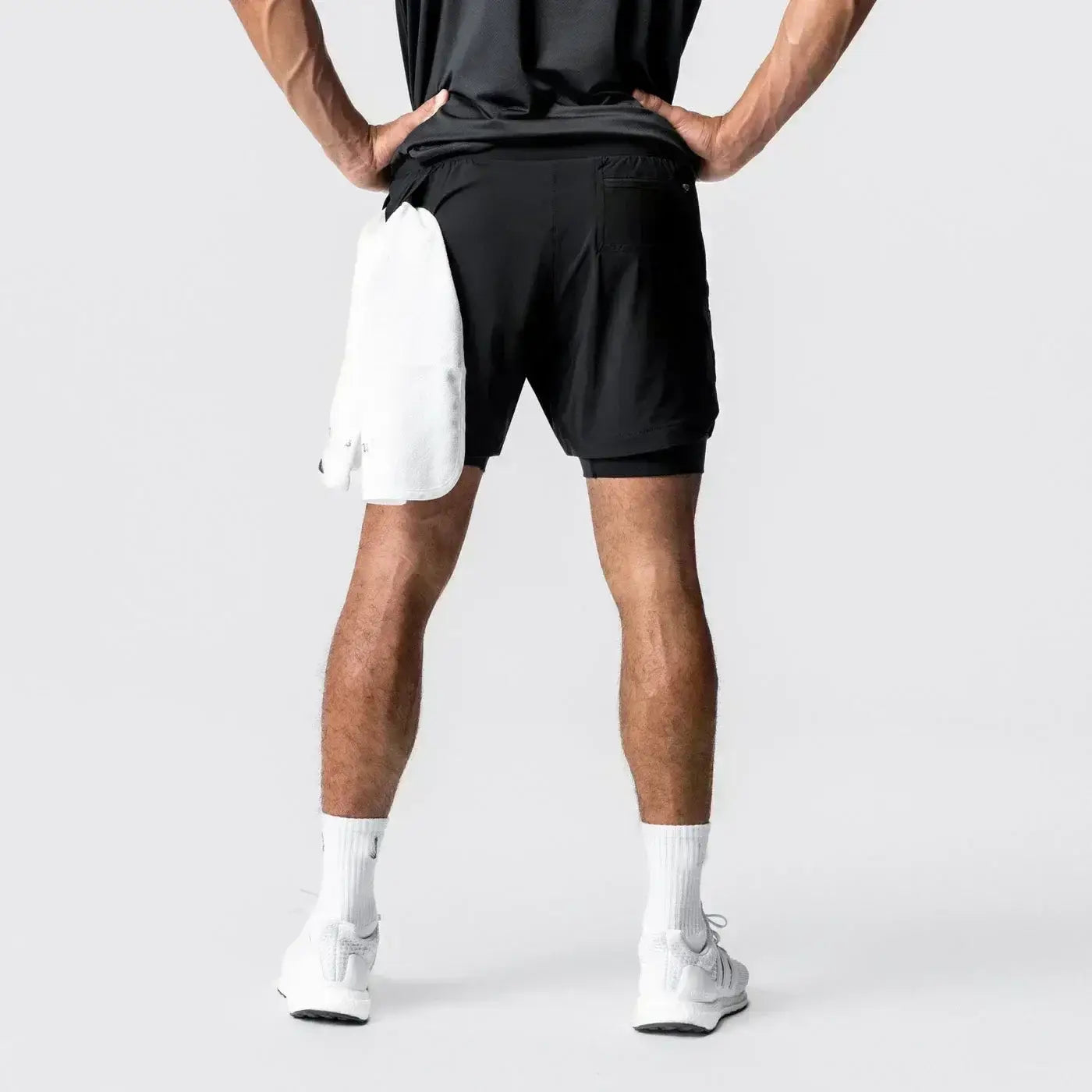 Pantalones cortos de entrenamiento para anime negros 2 en 1 para gimnasio de hombres con cintura elástica, mostrados desde la parte posterior, con una toalla blanca introducida en el bolsillo de la trabilla para la toalla.