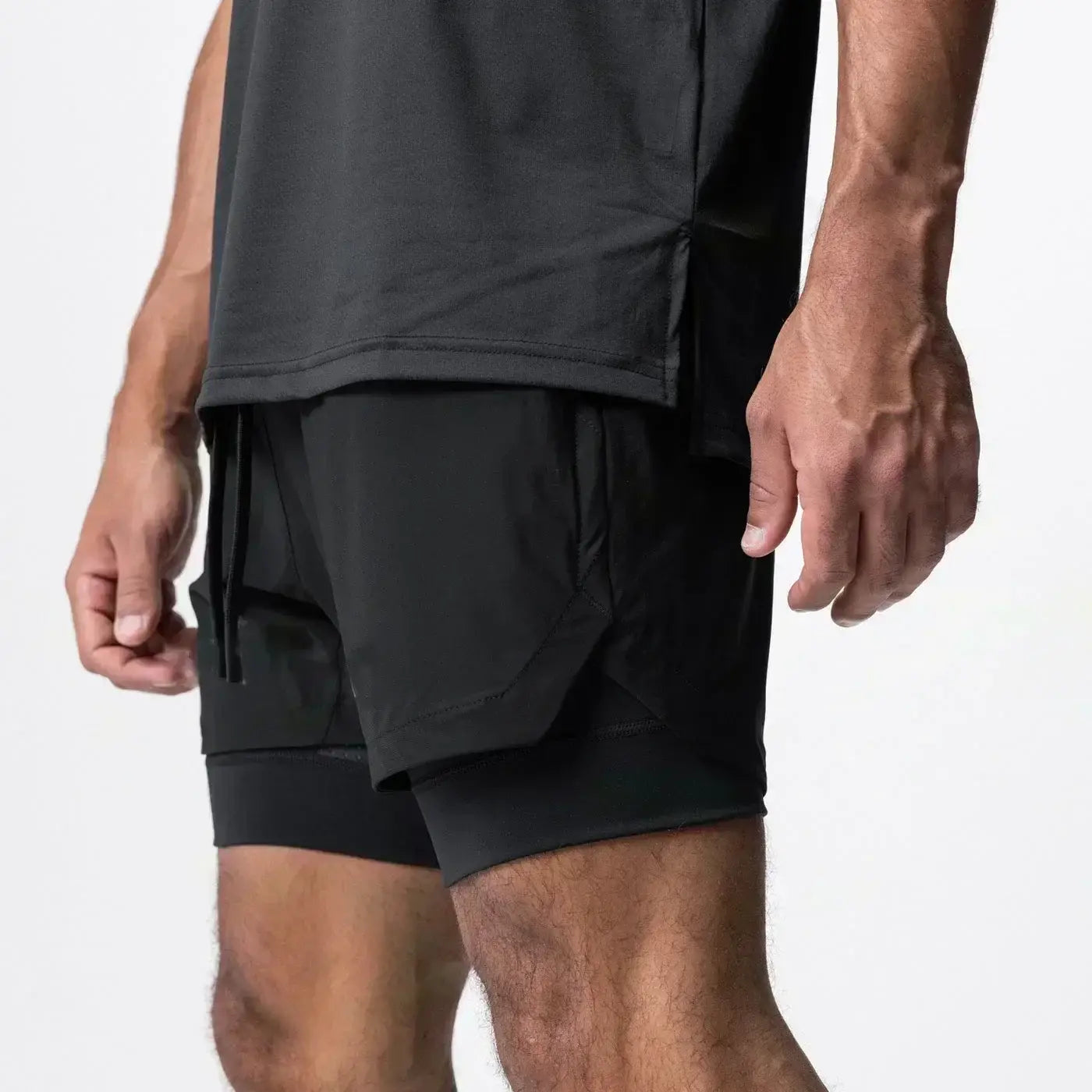 Pantalones cortos atléticos negros 2 en 1 para gimnasio de hombres con diseño en capas, bolsillos laterales y trabilla para la toalla que ofrece soporte durante los entrenamientos.