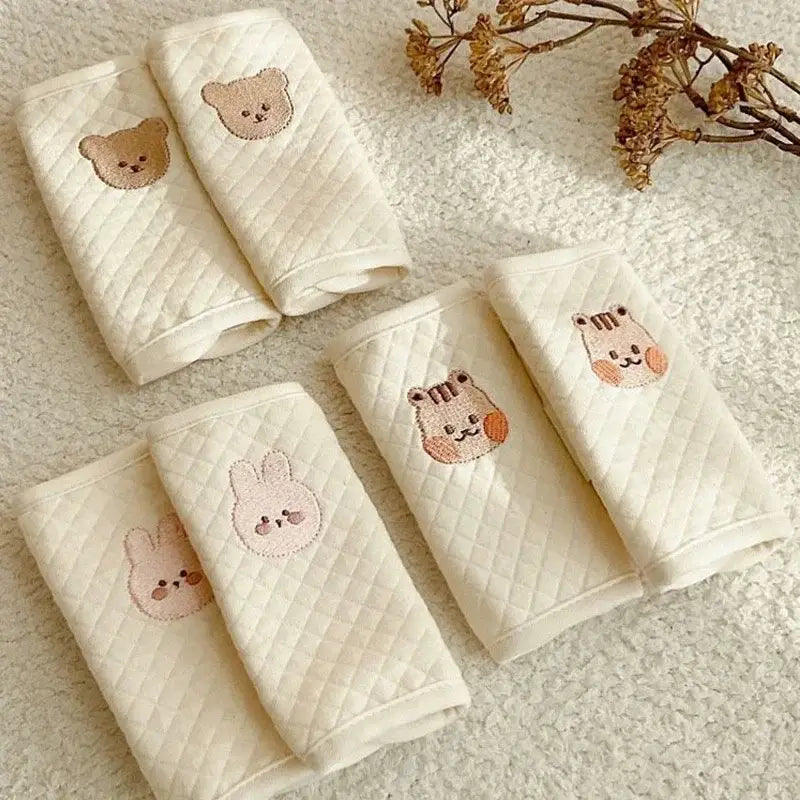 柔らかなパステルトーンで、刺繍のベア、トラ、ウサギの顔をあしらったクリーム色のキルティング加工ベビーミトン。ベビー用シートベルトカバーの肩パッドとして設計されています。