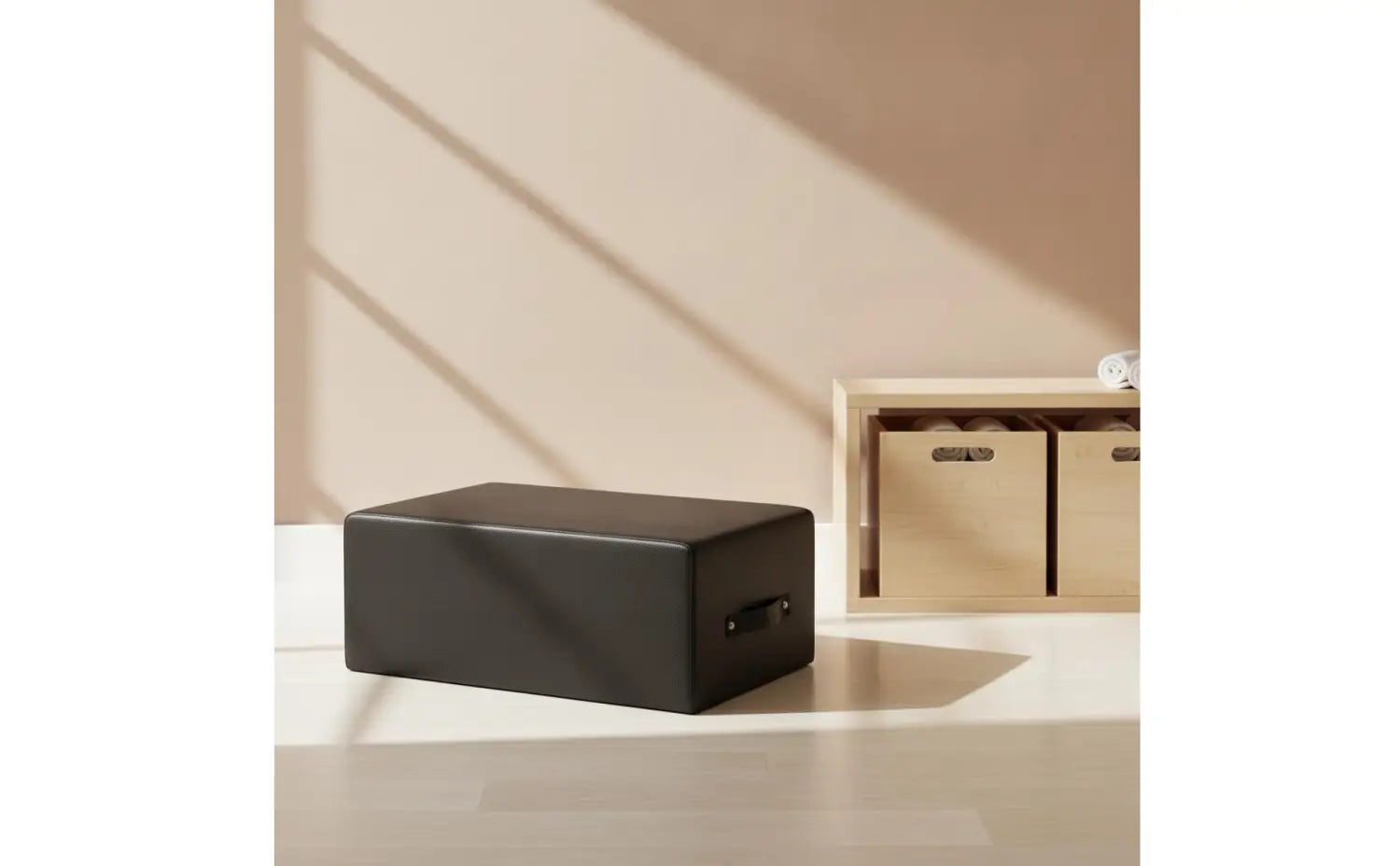 Schwarze rechteckige Pilates-Matte mit glatter, matter Oberfläche und kleinem Griff, dargestellt auf der gepolsterten Fitnessbox für Pilates und das Home-Gym.