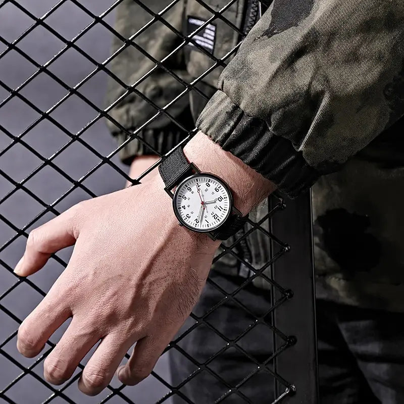 Militärisches Quarzarmbanduhr mit schwarzem Nylonarmband und weißem Zifferblatt mit schwarzen Stundenmarkierungen.