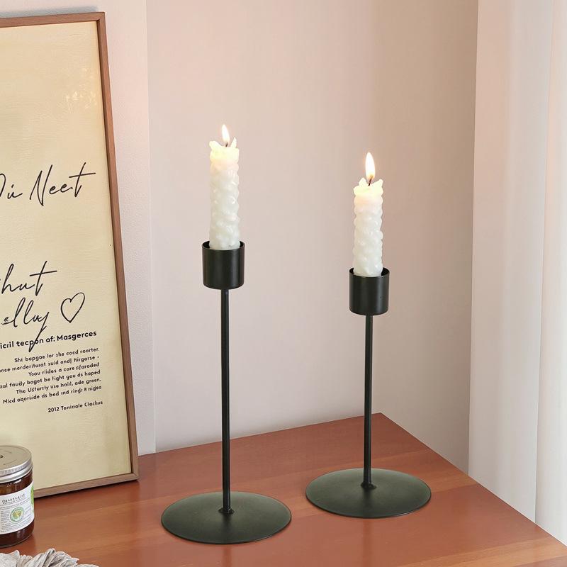 Black metal candle holders with slender stems and circular bases each holding a white textured taper candle for home decor in golden European style.