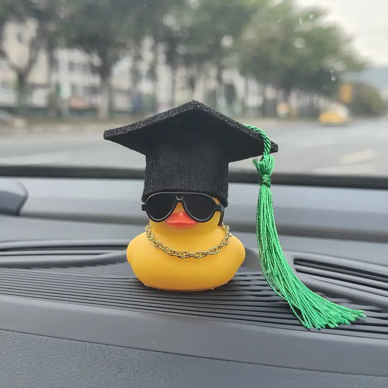 yellow rubber graduation duck car dashboard ornament wearing a black graduation cap with green tassel sunglasses and gold chain necklace