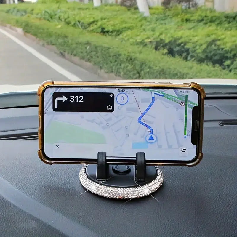 Un soporte para teléfono de automóvil con ventilación engalanado con pedrería brillante de color plateado, con carcasa negra y con acabado en dorado, que sostiene un iPhone que muestra una navegación.
