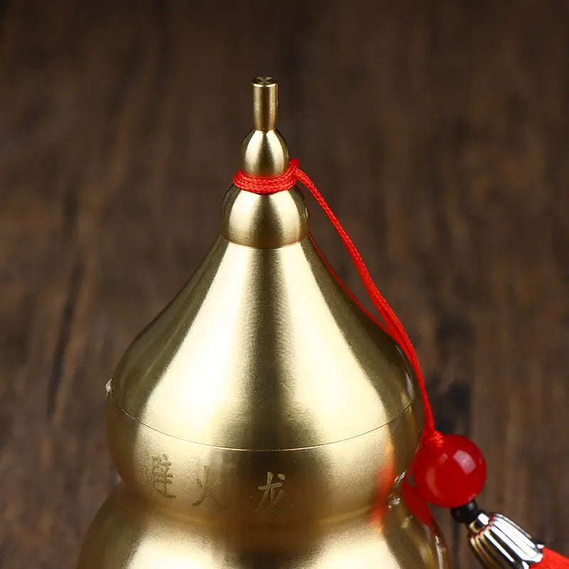 Golden brass gourd feng shui prosperity ornament with engraved Chinese characters adorned by a red cord and bead.