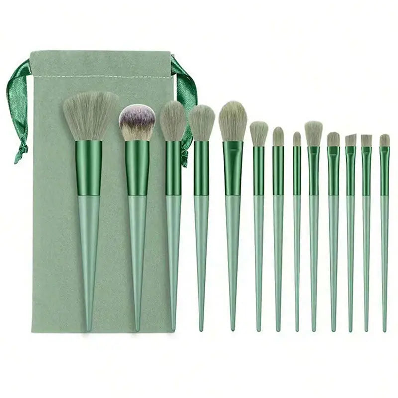 Set aus 12 professionellen Make-up-Pinseln mit grün lackierten Griffen und weichen hellfarbigen Borsten, ordentlich nebeneinander angeordnet neben einem passenden salbeigrünen Samtbeutel aus einem 13-teiligen Make-up-Pinselset.