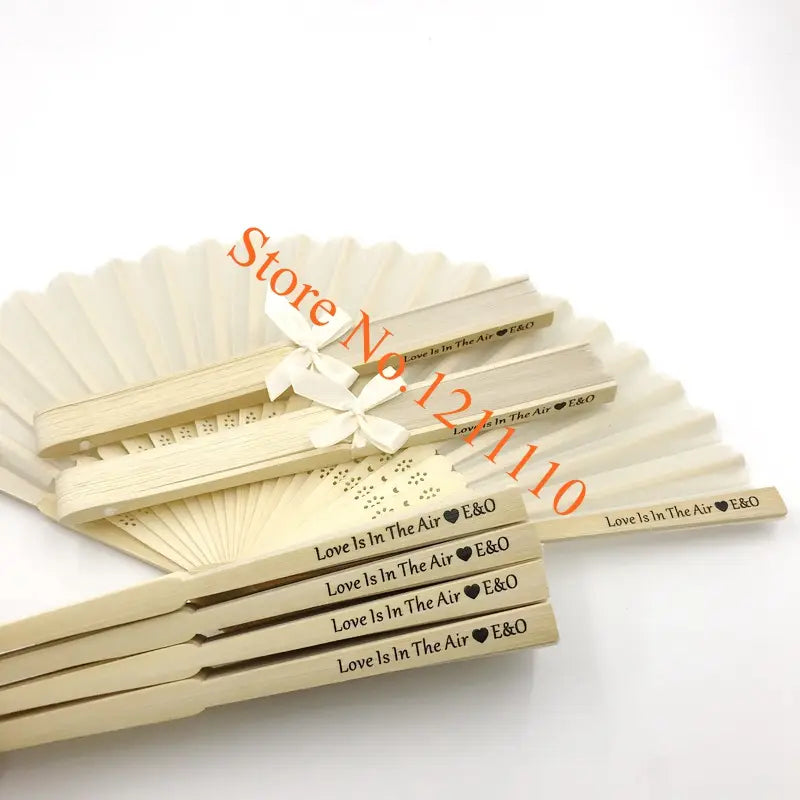 Beige wooden folding fans made of bamboo and silk with love is in the air e&o engraved on each blade tied with a white ribbon custom wedding hand fans personalized favors.