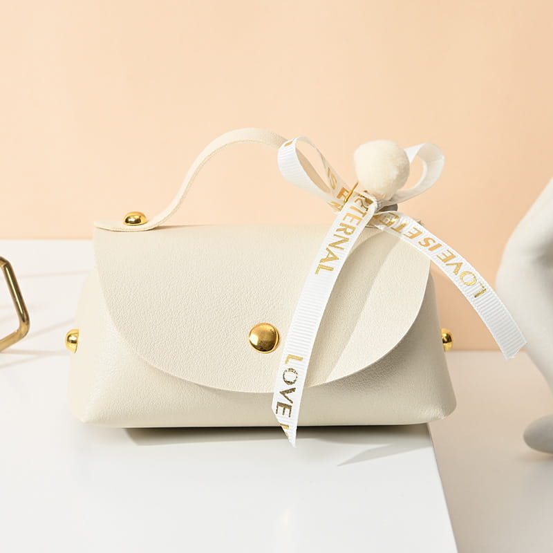 Mini pochette en faux cuir de couleur crème avec quincaillerie ton or et un ruban blanc noué en forme de nœud portant la mention « l’amour est éternel », conçue comme sac cadeau de mariage en cuir.