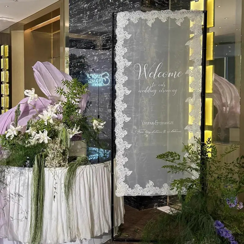 Ein zartes weißes Spitzenelement als Willkommensschild für die Hochzeit als Banner mit eleganter kursiver Schrift und den Namen des Paares für eine Hochzeitszeremonie.
