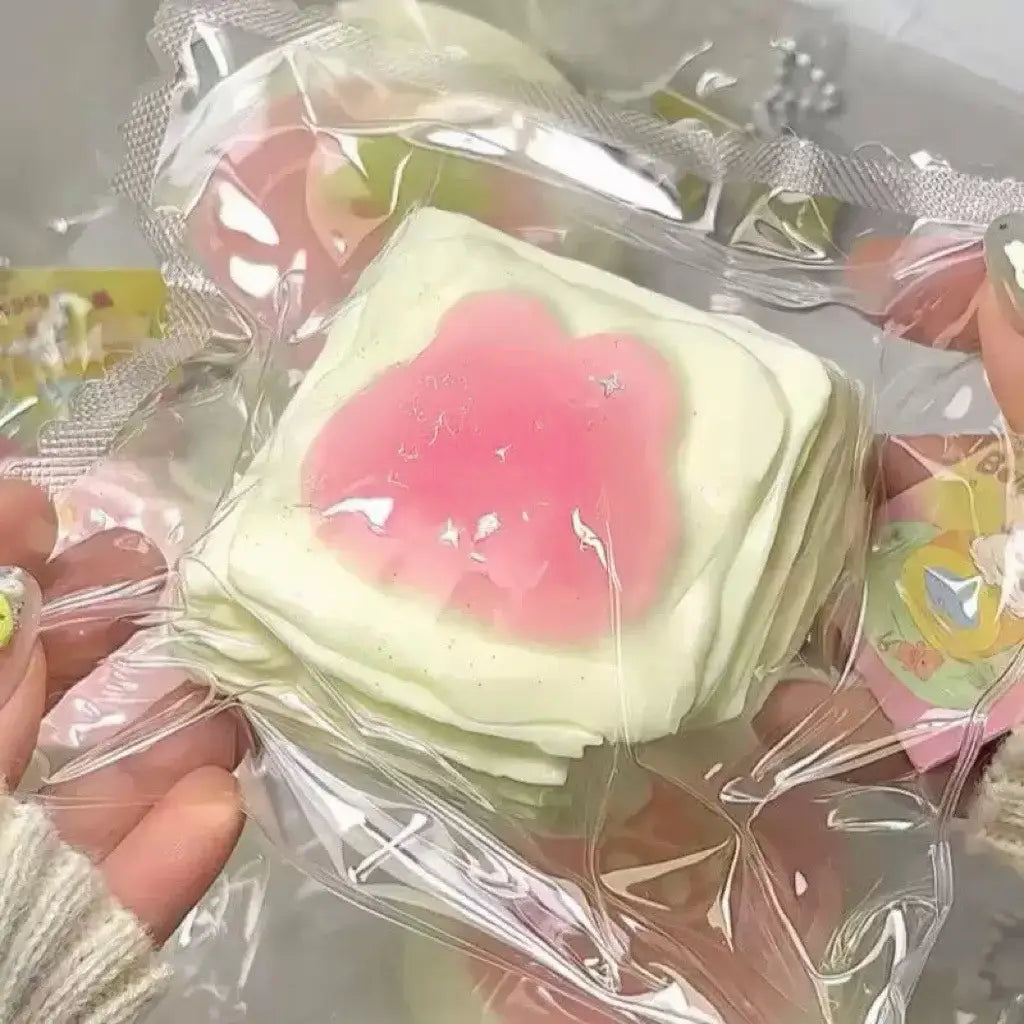 Une pile de jouets antistress « squeeze » carrés vert pastel, qui remontent lentement, avec un centre rose translucide de type gelée pour soulager le stress sensoriel.