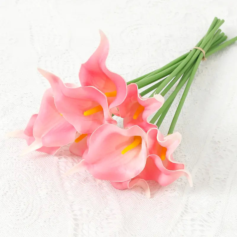 a delicate artificial calla lily flower bouquet with pink petals, yellow centers, and slender green stems tied with twine for home decor