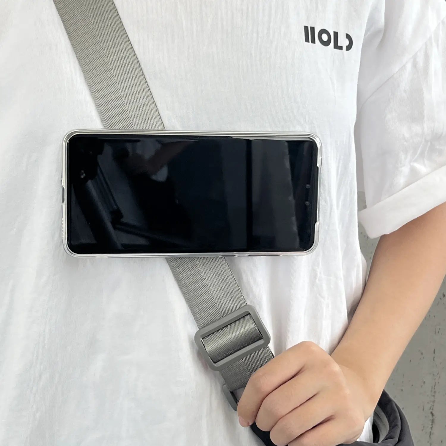 Graue Stoff-Magnet-Telefon-Rucksackclip Universalhalterung mit Schnalle, die ein Smartphone in einer transparenten Schutzhülle hält.