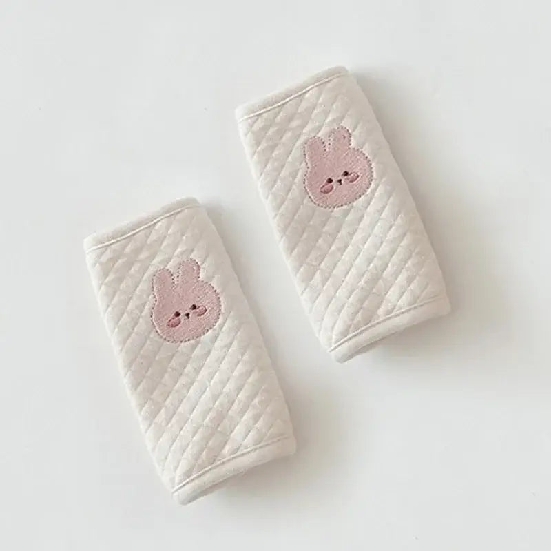 肩パッドのプロテクターとして、愛らしいピンク色の刺繍ウサギの顔をあしらったクリーム色のキルティング加工ベビー用シートベルトカバー