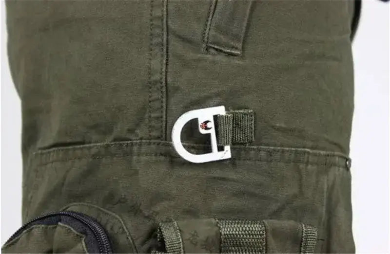Herren-Tactical-Cargo-Hosen aus Baumwolle mit Camo-Jogger-Optik mit einer weißen Metall-Schnalle mit schwarzem und rotem Logo auf olivgrünem Stoff.