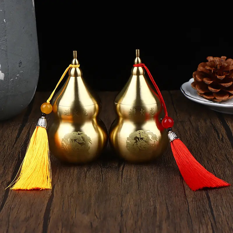 Two golden metallic brass gourd feng shui prosperity ornaments with engraved Chinese characters and decorative tassels in yellow and red.