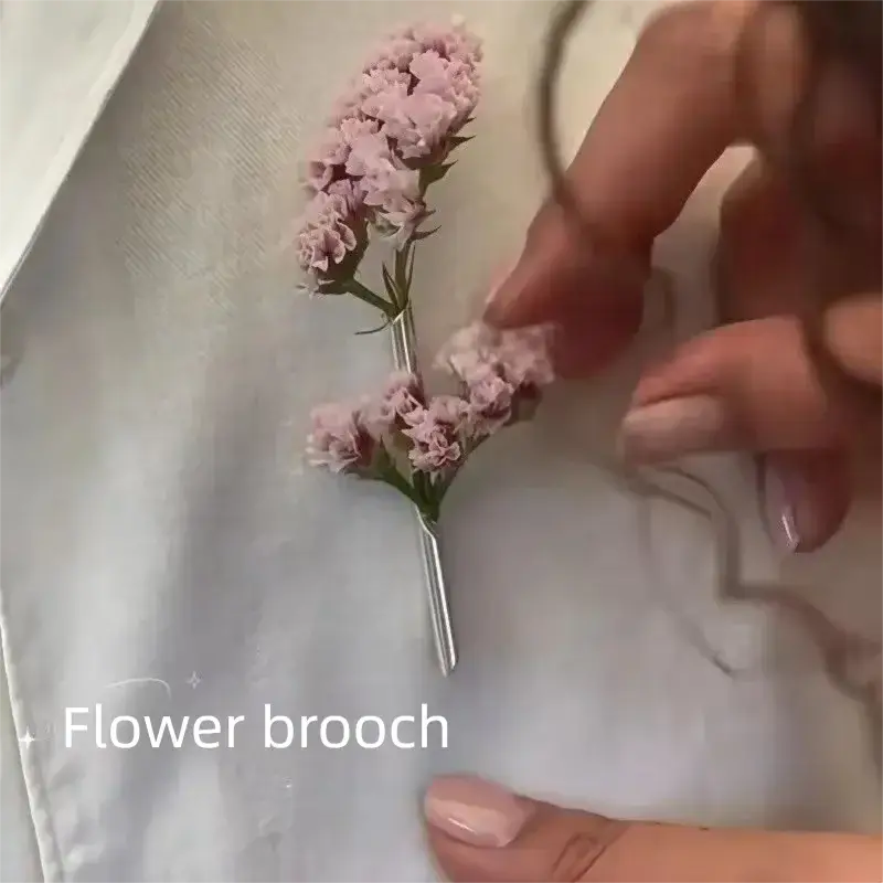 Eine zarte rosafarbene Broschennadel-Blume mit winzigen Blüten und einer schlanken silberfarbenen Nadel als kreatives Corsage-Zubehör.