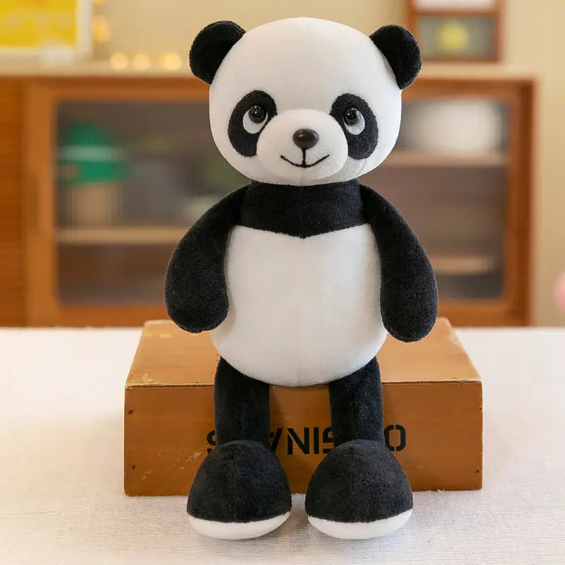 Mignon ours panda en peluche rembourré noir et blanc, fabriqué dans un tissu doux, assis bien droit sur une boîte en bois, présenté parmi les jouets lion éléphant tigre de la forêt.