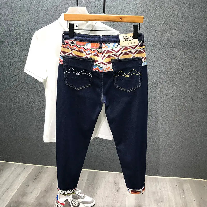 Men slim fit stretch embroidered white denim jeans featuring dark blue denim with a colorful geometric patterned waistband and rolled cuffs.