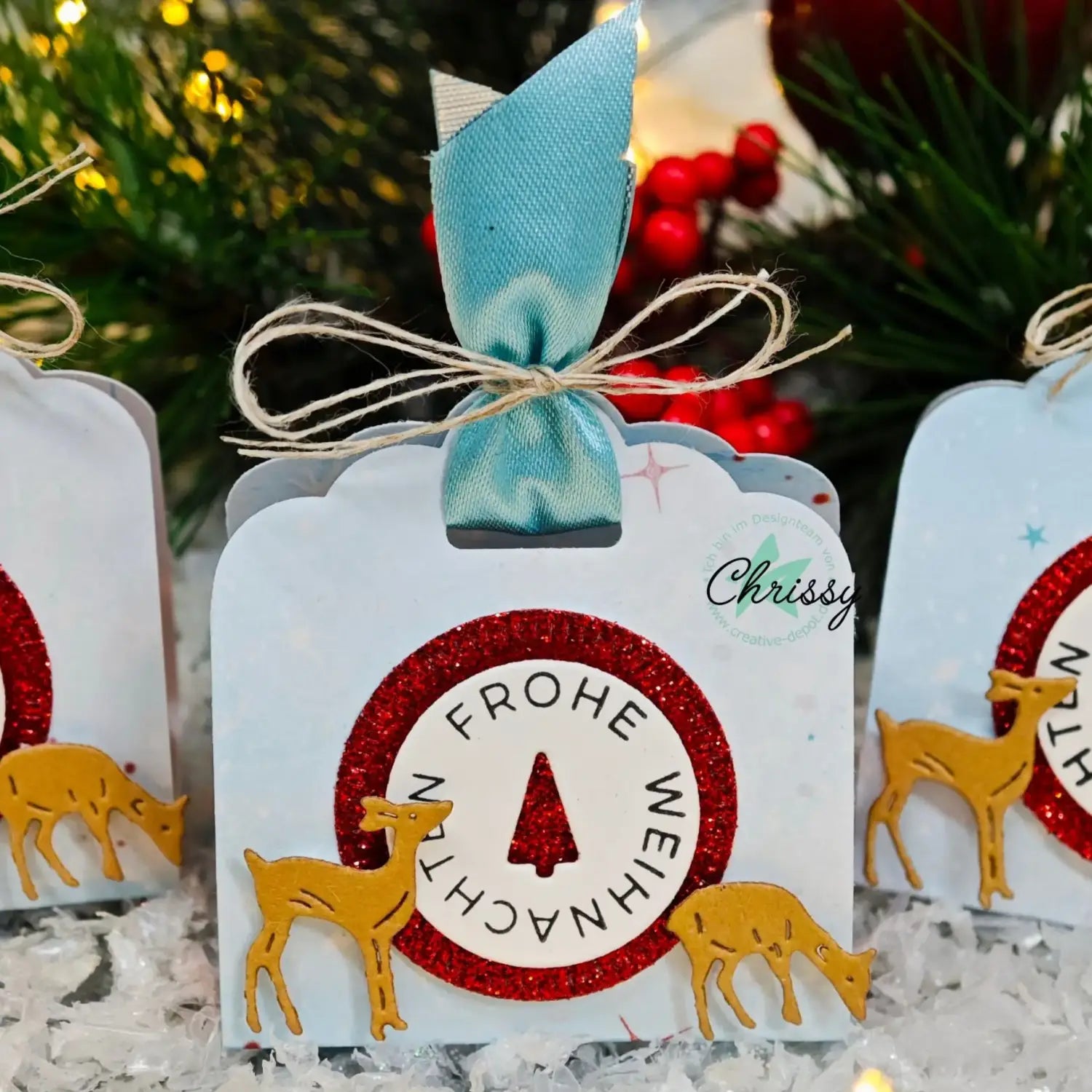 a festive white christmas gift tag featuring a red glittery circle and gold metal reindeer cutouts with the german phrase frohe weihnachten around a tree silhouette created using winter animal metal cutting dies for scrapbooking.