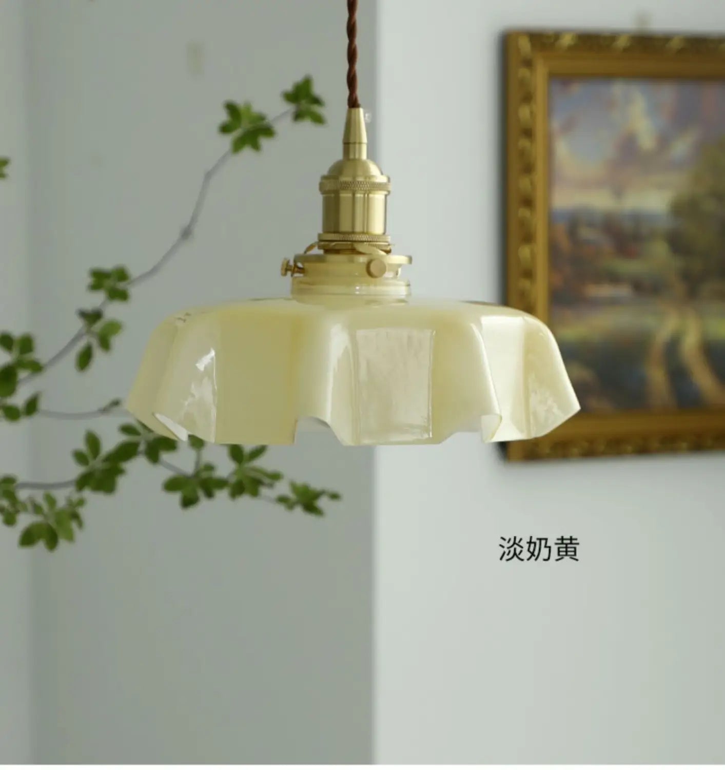 Un luminaire délicat suspendu à jupe florale en verre jaune pâle avec une tête de lampe en cuivre et un cordon tressé visibles depuis un angle avant.