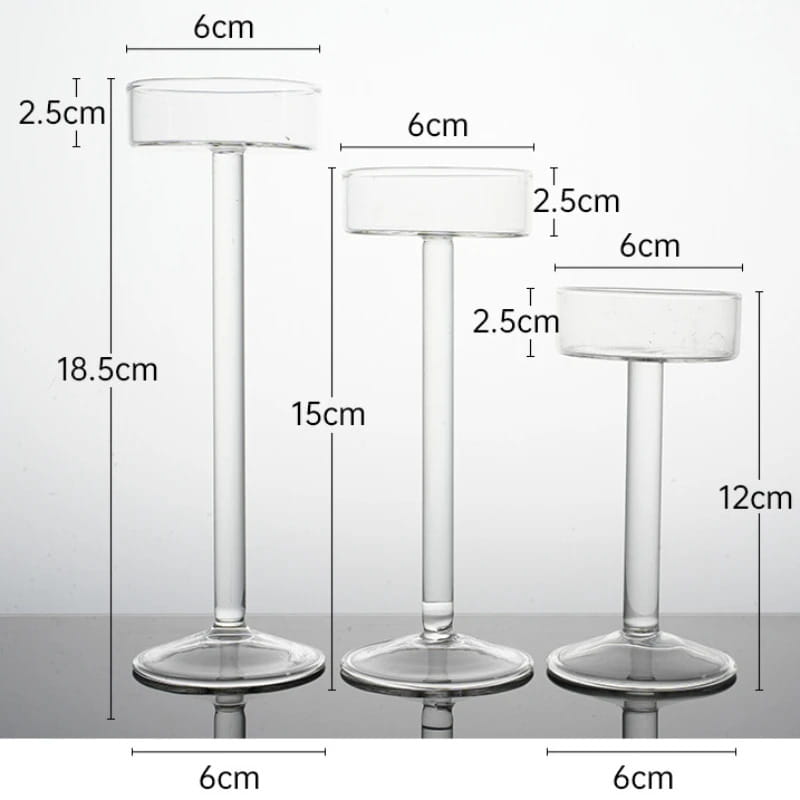 Tres portavelas de pilar de vidrio transparente, con partes superiores cilíndricas, tallos esbeltos y bases circulares, para una decoración moderna de mesa.