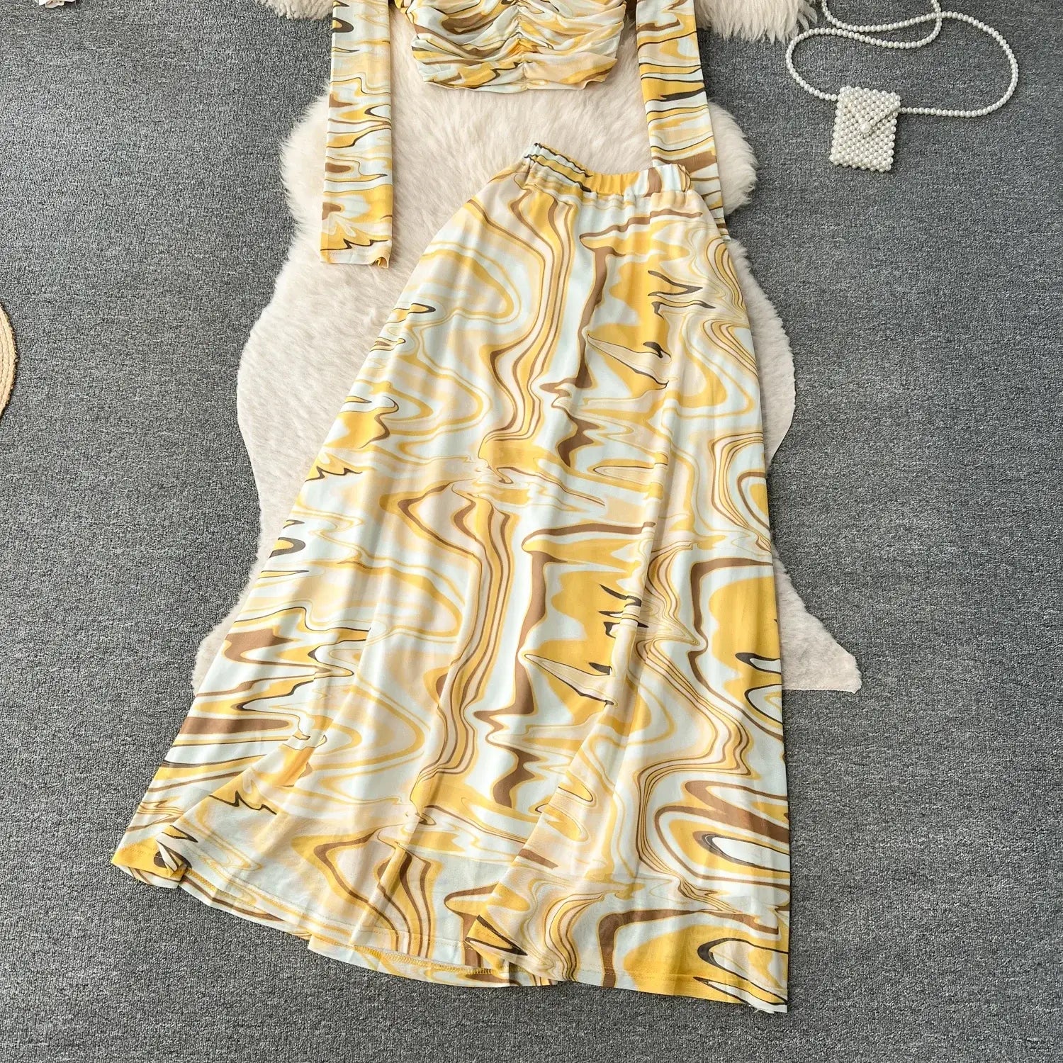 A two piece mesh skirt set with a flowing yellow white and brown marbled patterned maxi skirt and matching top featuring an elastic closure.