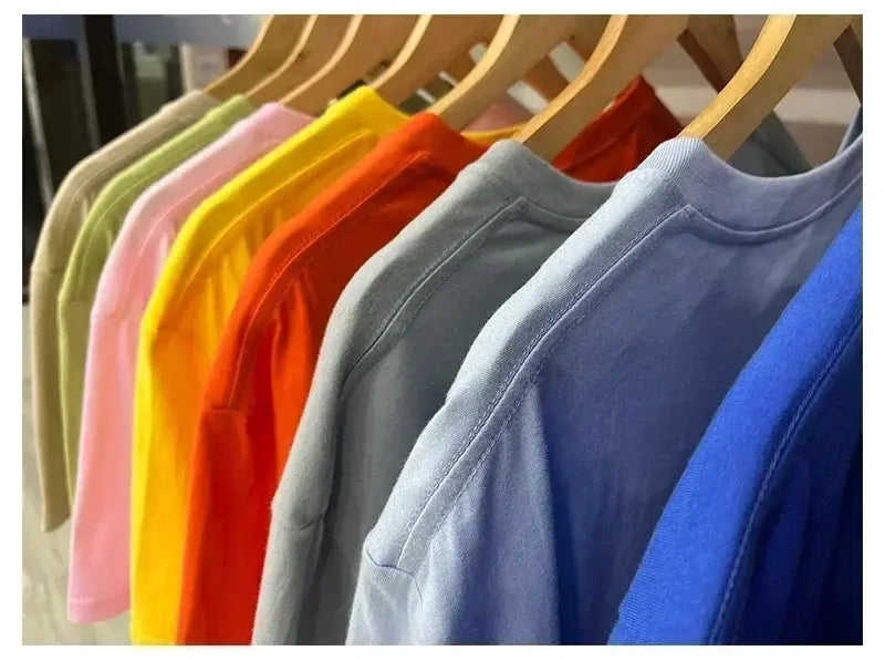 Une rangée de t-shirts en coton vintage à motif de voiture de muscle, colorés, dans des tons pastel et éclatants, suspendus avec soin à des cintres en bois.