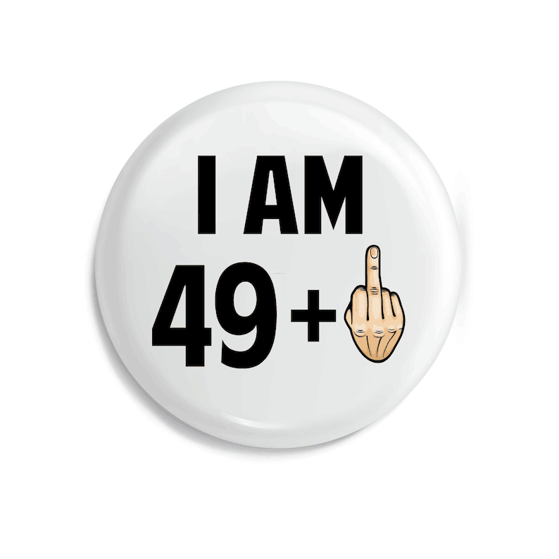badge de broche émaillé circulaire blanc avec du texte noir indiquant « j’ai 49 ans et plus » et une gestuelle de main en forme de dessin, conçu comme un cadeau amusant d’anniversaire marquant une étape d’âge.
