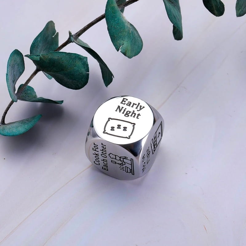 Silver metallic six-sided stainless steel food decision die engraved with phrases and illustrations including early night for couples date night.