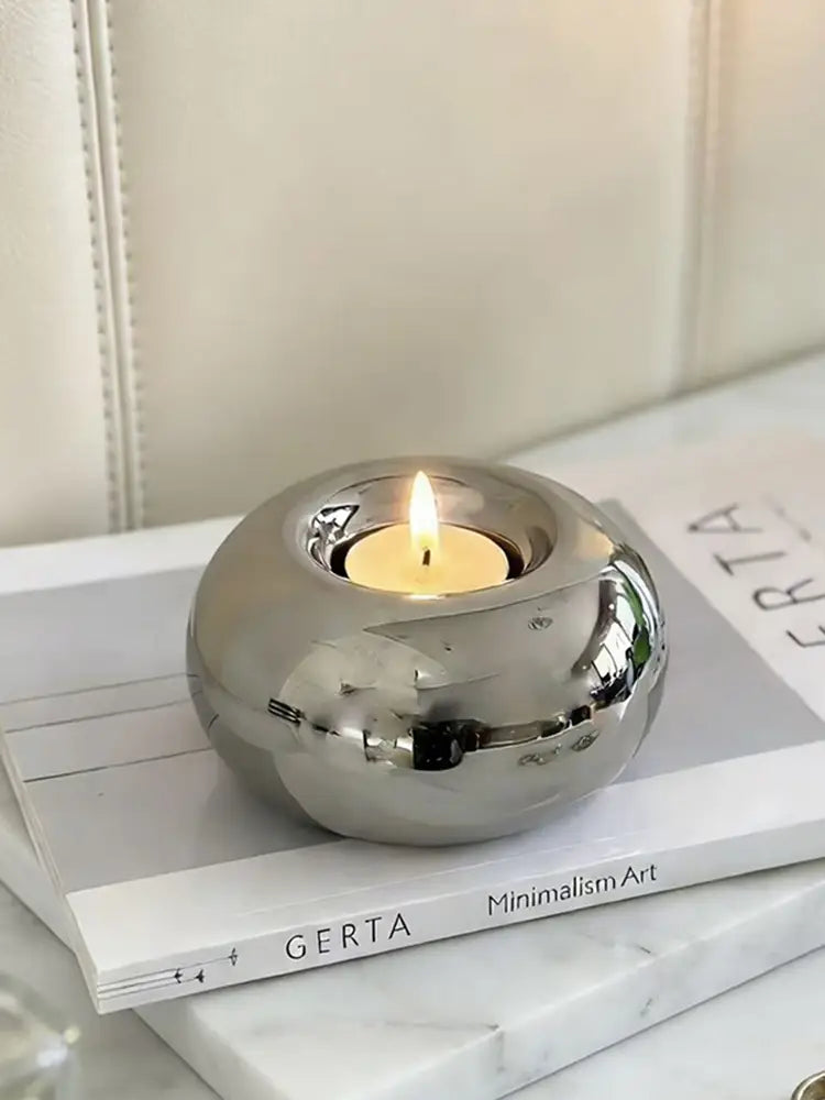 A sleek spherical silver ceramic candle holder with a polished metallic finish cradles a lit tea light.