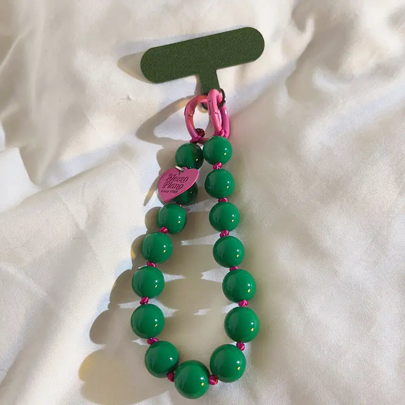 Una vibrante correa de muñeca para teléfono con cuentas verde, con acentos rosados y una etiqueta con forma de corazón mostrada desde la parte frontal.