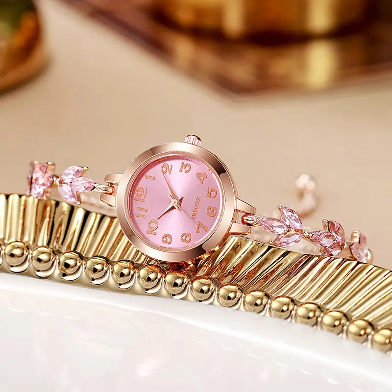 A delicate rose gold women rhinestone quartz watch with a pink dial and matching pink gemstone accents on a crystal leaf bracelet.