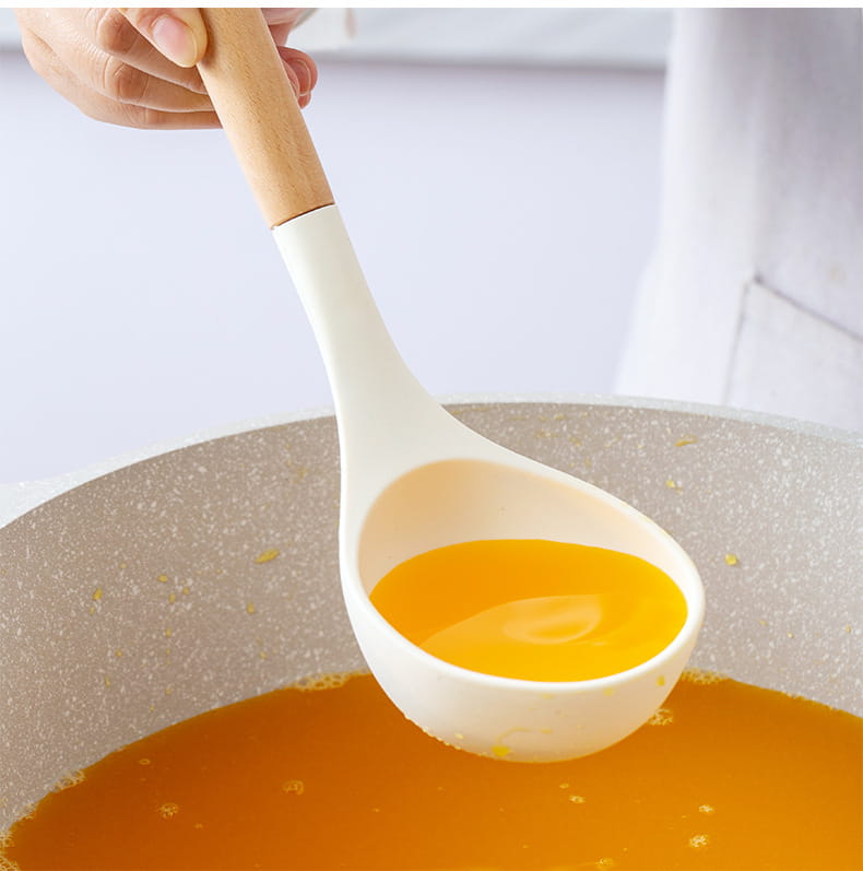 White silicone kitchen ladle with a wooden handle holding golden broth from the white silicone kitchen utensils set.