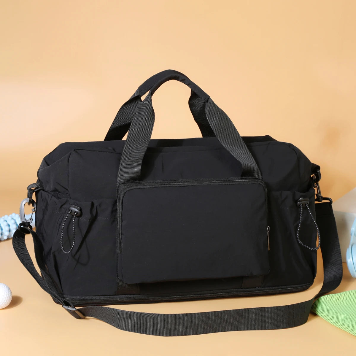 Sac de voyage duffel en nylon noir avec doubles poignées supérieures et bandoulière amovible, doté d’un système de bagagerie légère extensible.
