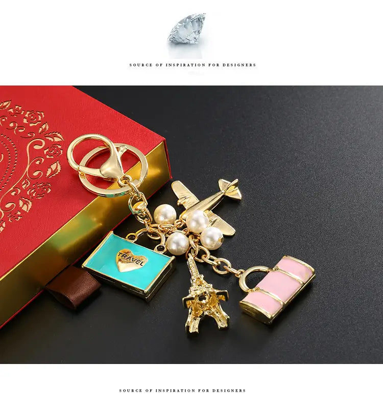 Llavero de viaje en tono dorado con un avión en miniatura, cuentas de perlas, colgante de Torre Eiffel y un colgante de maleta de esmalte con inscripción de viaje.