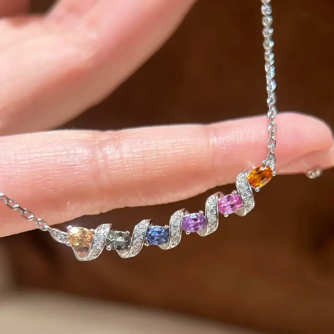 Un délicat collier en argent présentant un pendentif géométrique tourbillonnant avec cinq pierres précieuses ovales colorées serties en bordure, de couleur jaune, rose, violette, bleue et orange, chacune entourée de minuscules diamants.