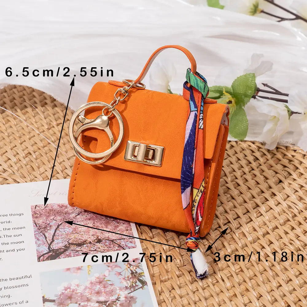 Orange miniature handbag keychain with gold-tone hardware and a colorful silk scarf ribbon strap.