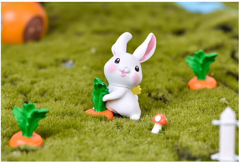 Figurine miniature en résine céramique blanche de lapin, avec des oreilles internes et des joues roses, tenant une carotte verte pour la décoration d’un jardin féerique.