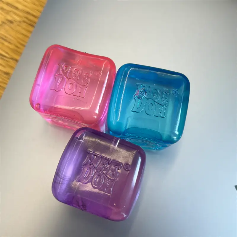 three translucent cube-shaped ice cubes in pink, blue, and purple with the kee do logo embossed on the front viewed as a needoh nice fidget toy needoh nice cube