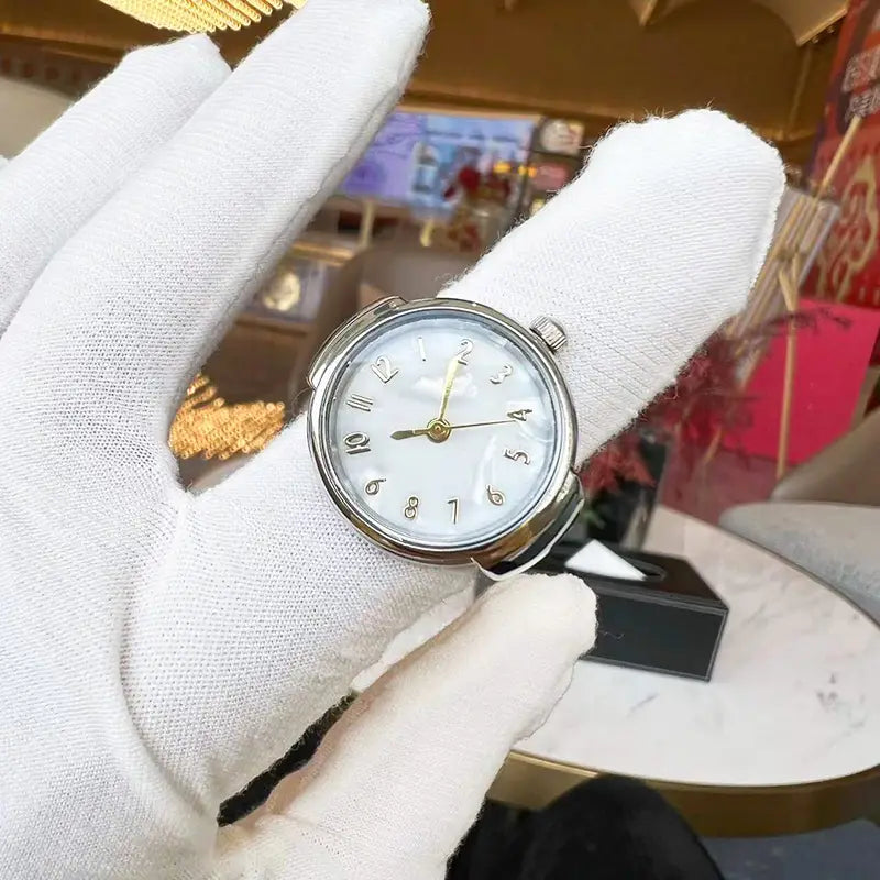 A silver-toned ring watch quartz finger jewelry unisex gift featuring a white dial with black arabic numerals and gold-tone hands.