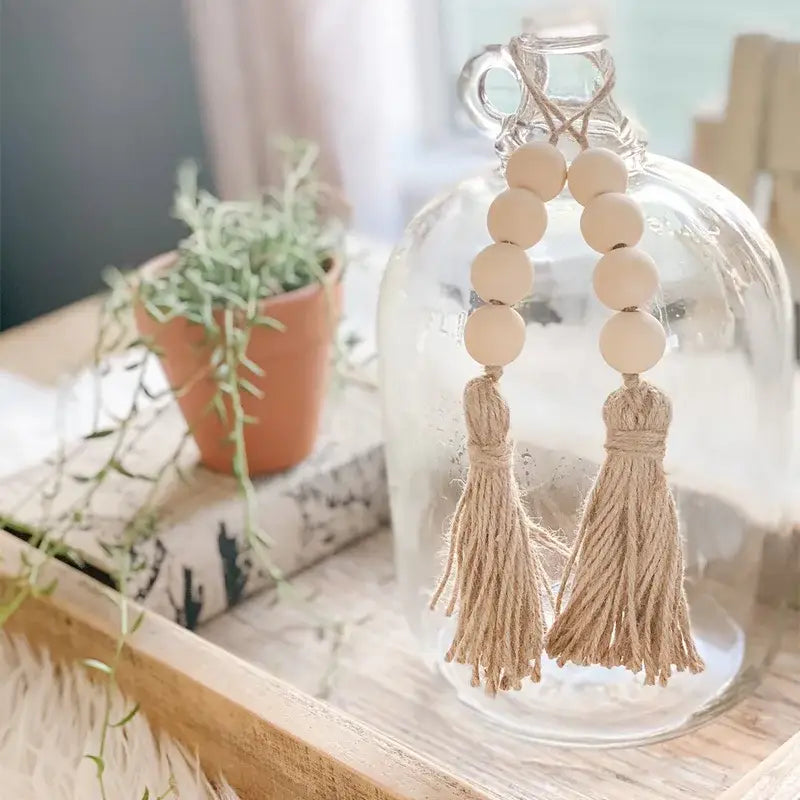 Beiger hölzerner Perlen-Tassel-Girlandenanhänger, der von einer Glasvase aus Naturholz hängt.