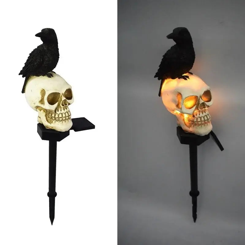 Un cuervo negro posado sobre un cráneo blanco con detalles dorados, iluminado desde el interior y que forma parte de la lámpara de jardín solar con cráneo y cuervo.
