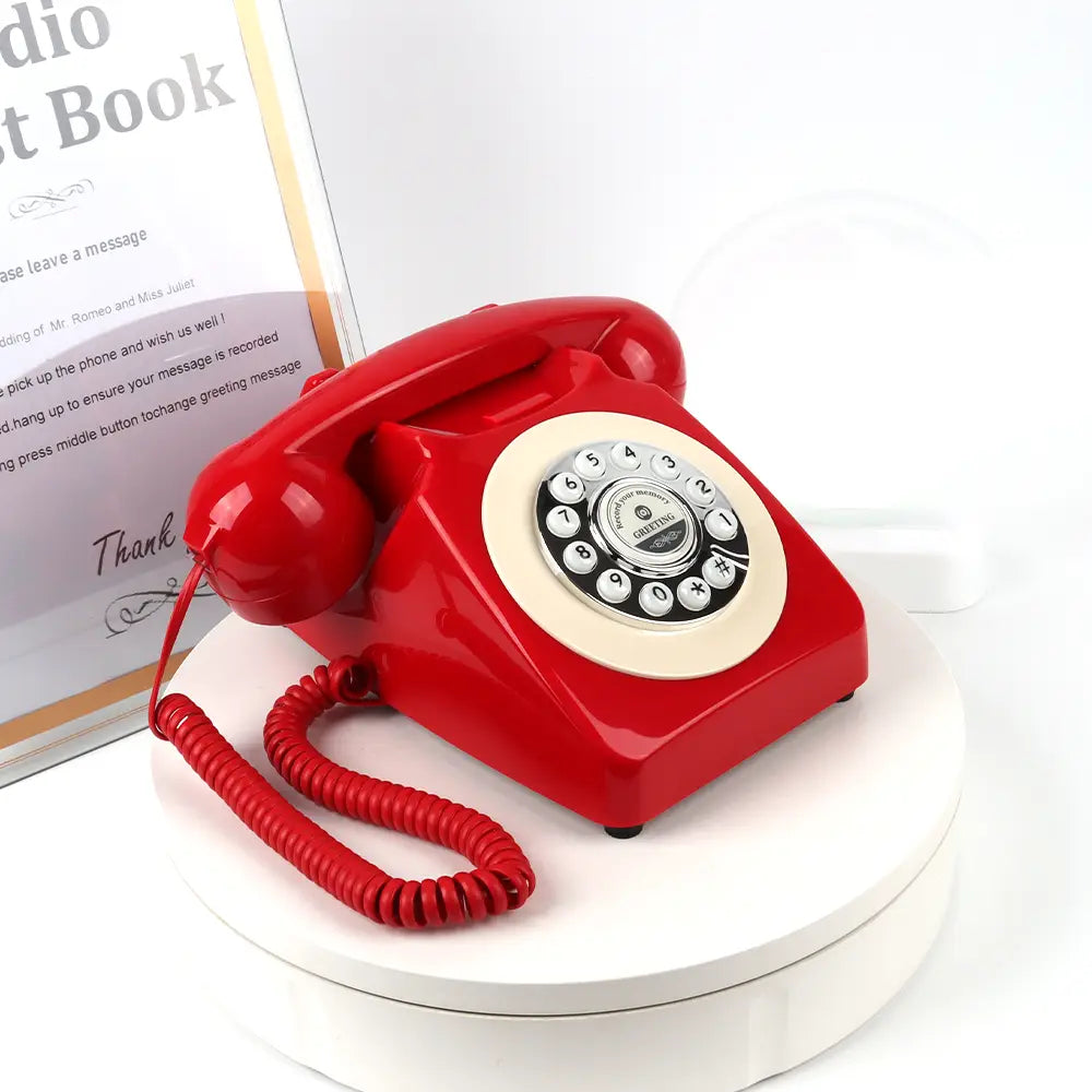 Teléfono de registro de audio antiguo para bodas y eventos con un teléfono rotatorio rojo vibrante con dial circular color crema, números con acabado de tono plateado y un cable en espiral.