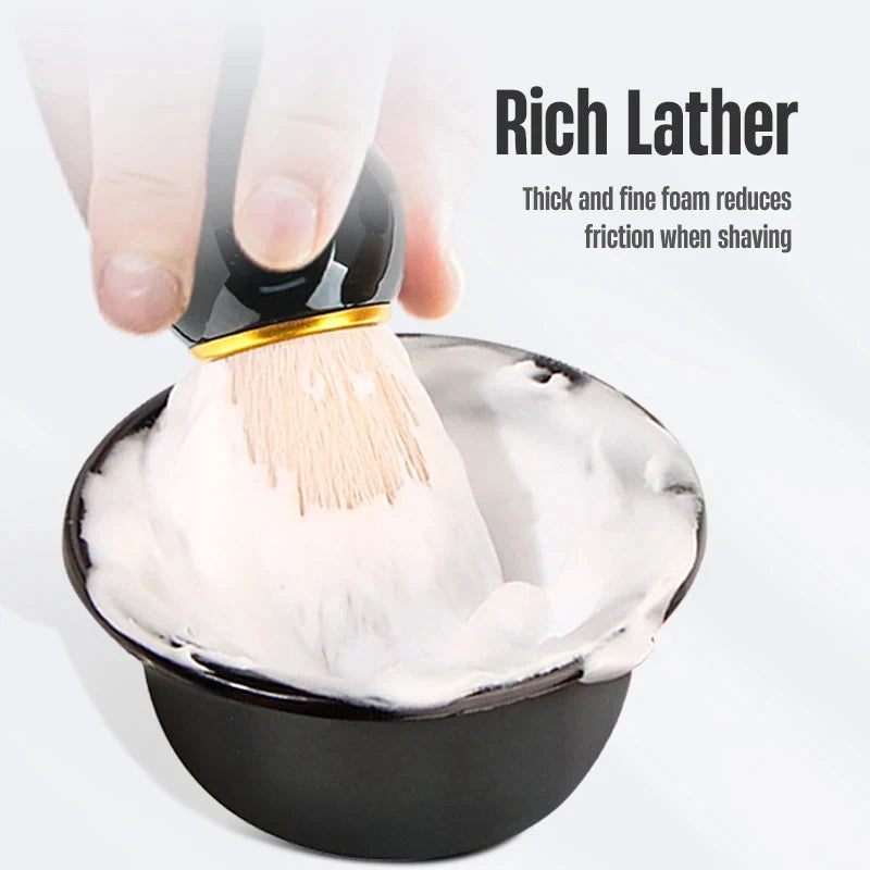 Black shaving brush with gold trim and light bristles dipped into white lather in wet shaving bowl kit