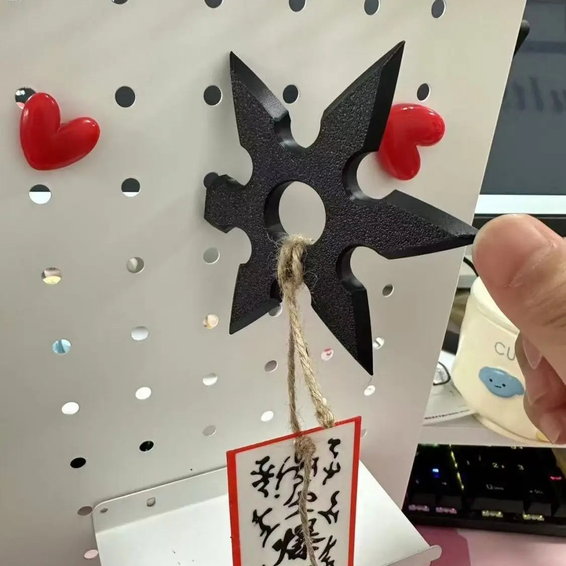 Ninja-Shuriken-Spielzeug aus schwarzem Kunststoff in Form eines Sterns, als Kühlschrankmagnet, mit rauer Oberfläche, flankiert von zwei roten Herzmagneten.