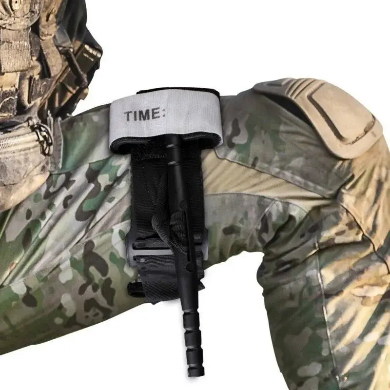 Schwarzes taktisches Kampf-Tourniquet mit einem grauen Gurt, der das Wort „time“ in schwarzer Schrift trägt, an taktischer Ausrüstung befestigt, für die Notfallmedizin.