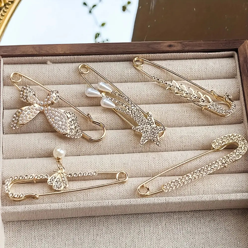 Broches épingles de sûreté ton doré, rehaussées de rhinestones scintillants, de nœuds, de perles et d’étoiles, conçues comme pinces à foulard pour femmes.